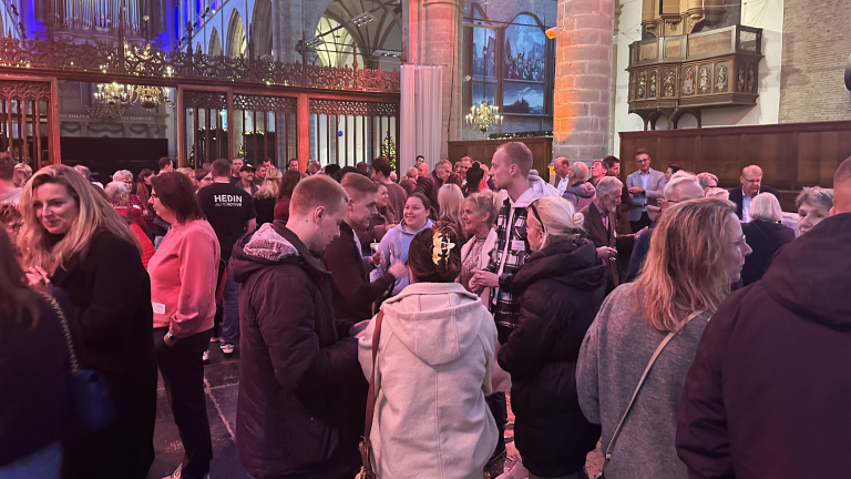 Mensenmassa in een kerk met kleurrijke verlichting en grote kroonluchters.