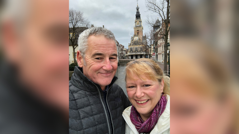 Een man en vrouw poseren voor een foto met op de achtergrond een historisch gebouw met een toren.