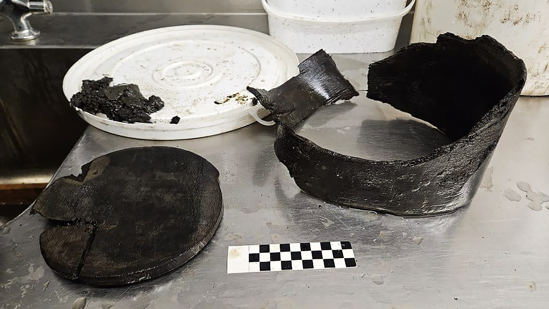 Een houten artefact op een metalen tafel met een zwart-wit schaalblok ernaast.