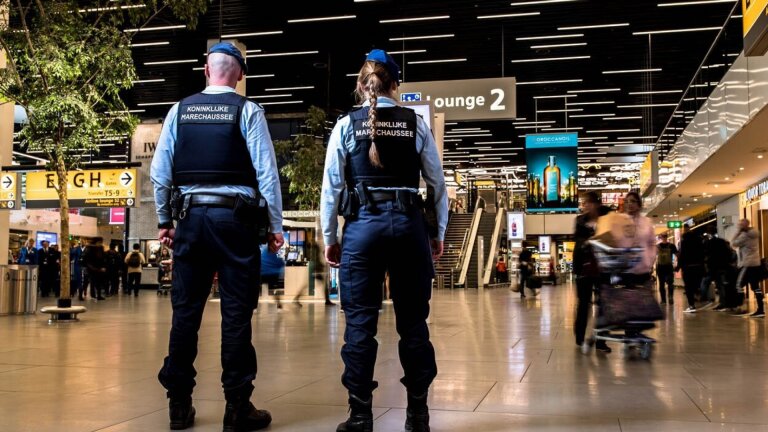 Twee marechaussees in uniform staan op de luchthaven, in de vertrekhal nabij lounge 2.