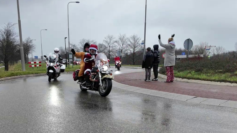 Motorrijders in kerstkostuums rijden langs terwijl mensen langs de weg ze toejuichen.