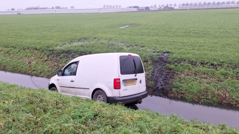 Witte bestelauto half in een sloot naast een grasveld.