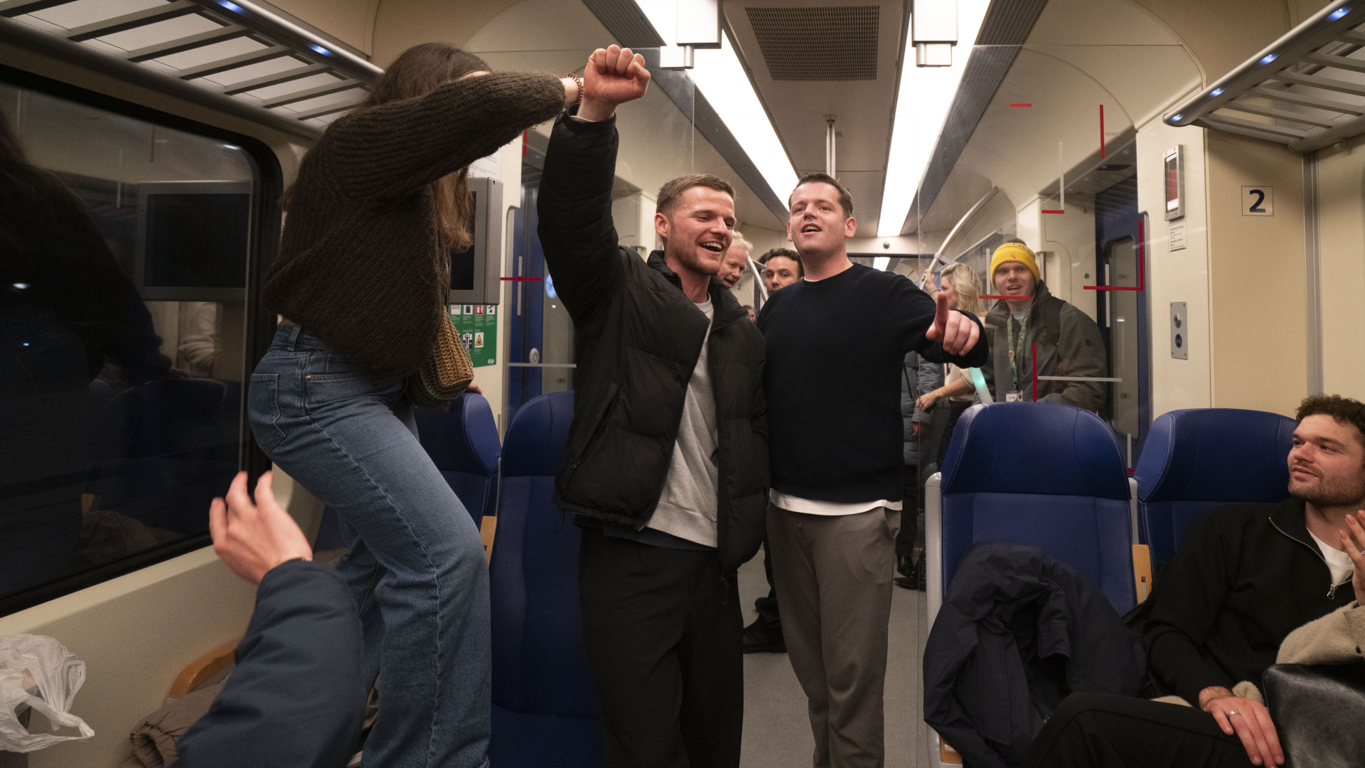 Mensen vieren feest in een trein, met enkele personen die glimlachen en zingen.