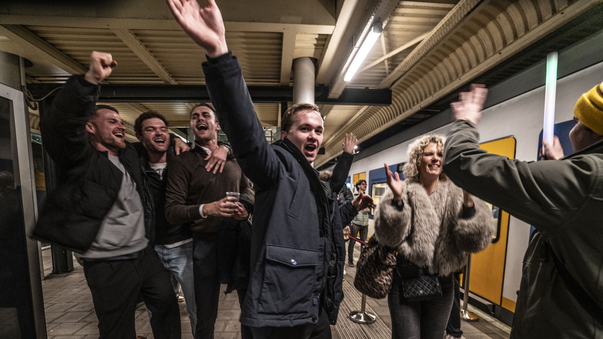 Mensen juichen en vieren feest op een perron van een treinstation.