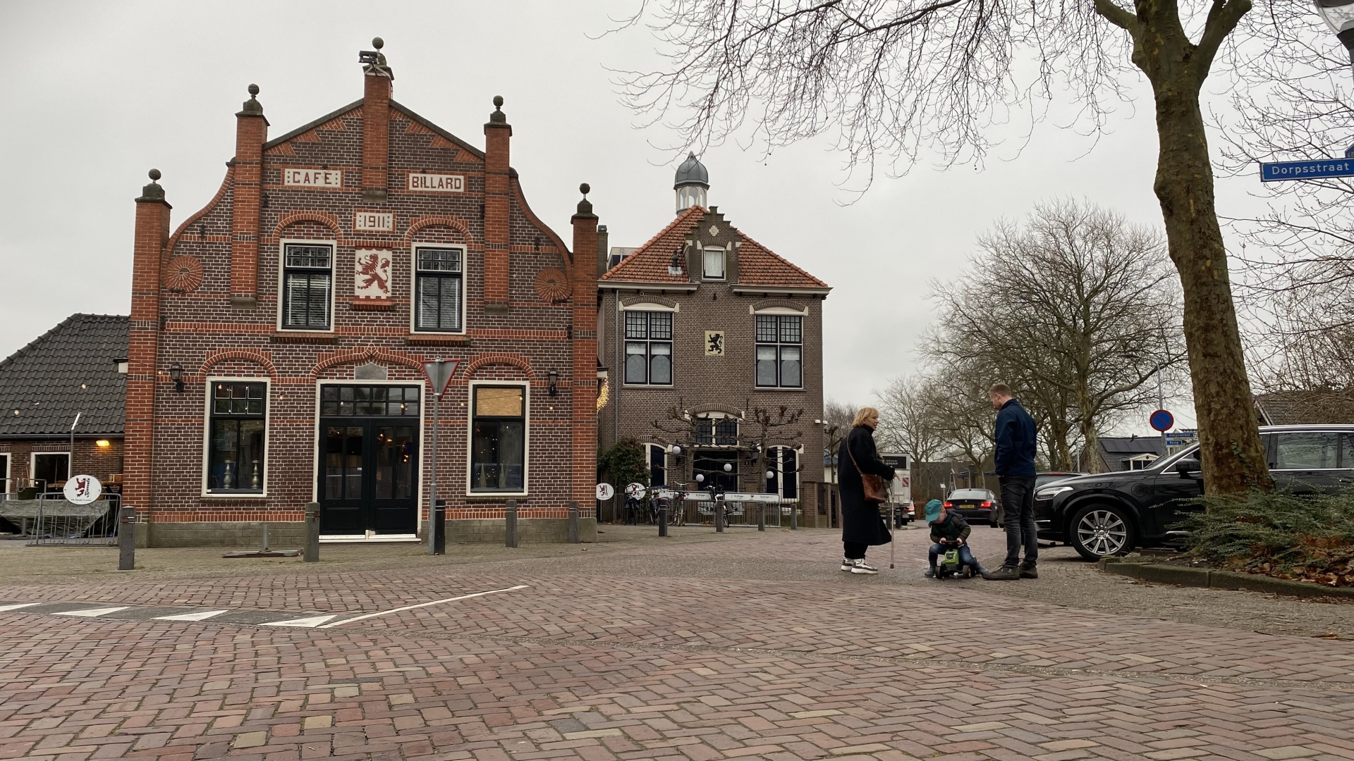 Historisch bakstenen gebouw genaamd "Café Billard" met mensen op straat in een dorp.