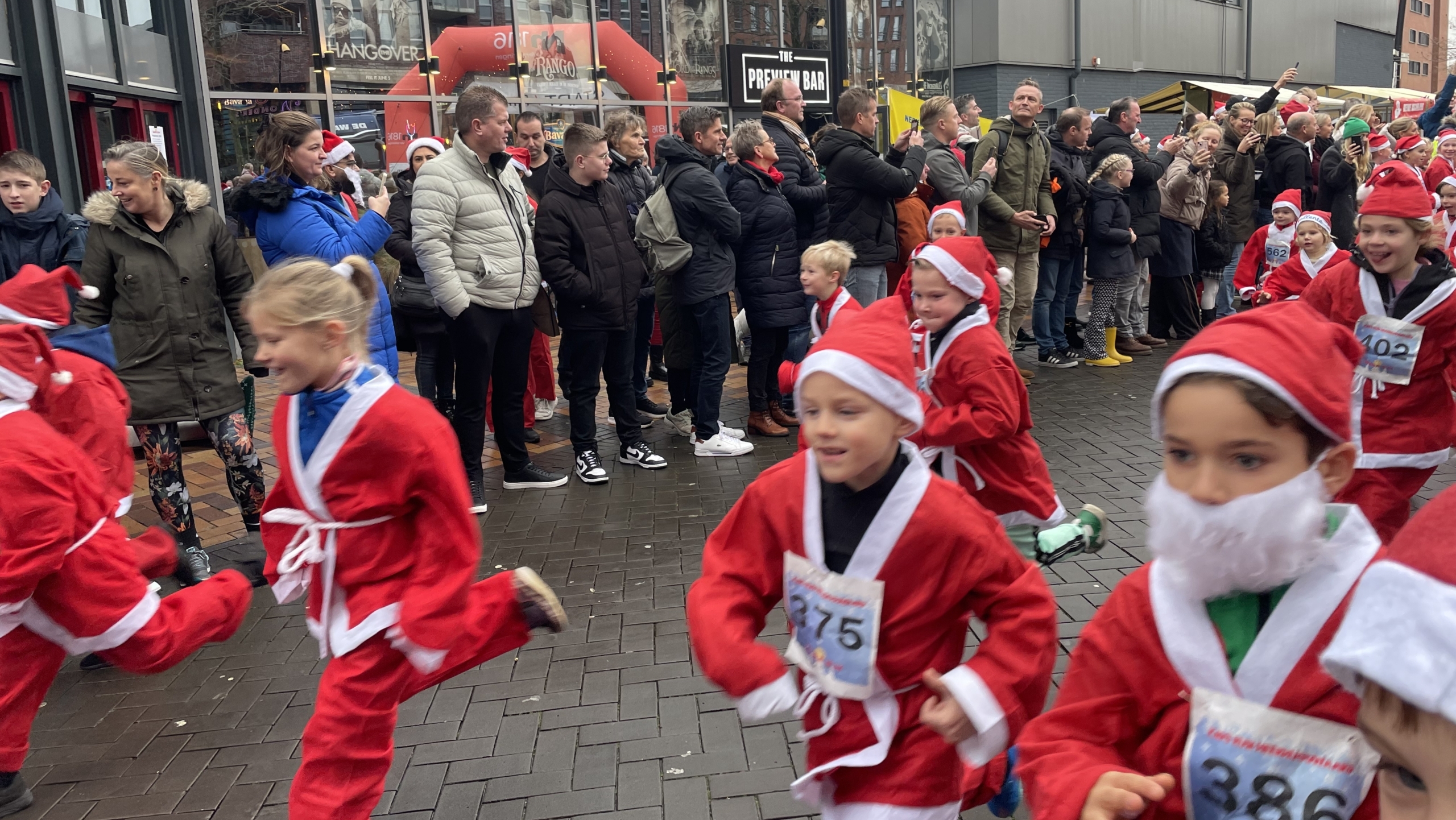 Kinderen verkleed als kerstmannen rennen tijdens een evenement terwijl toeschouwers toekijken.