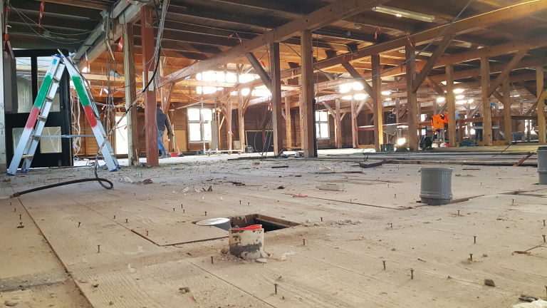 Industriële ruimte in renovatie met houten balken en vloer, metalen trap en bouwmaterialen.