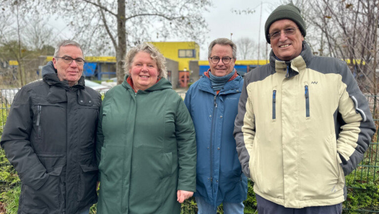 Vier mensen in warme jassen poseren buiten op een bewolkte dag.