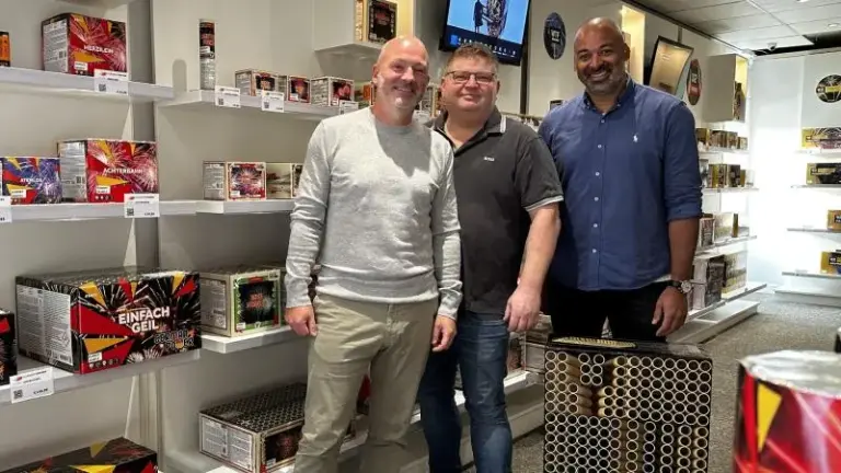 Drie mannen staan in een winkel met vuurwerkdozen om hen heen.