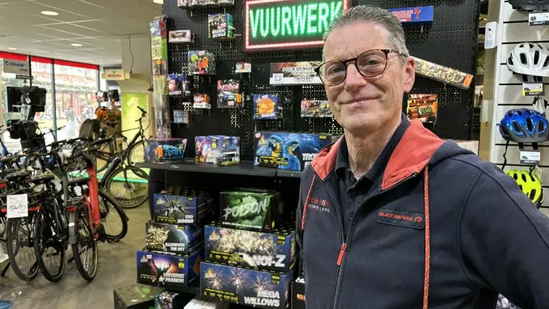 Man voor een display van vuurwerk in een winkel, omringd door fietsen en fietshelmen.