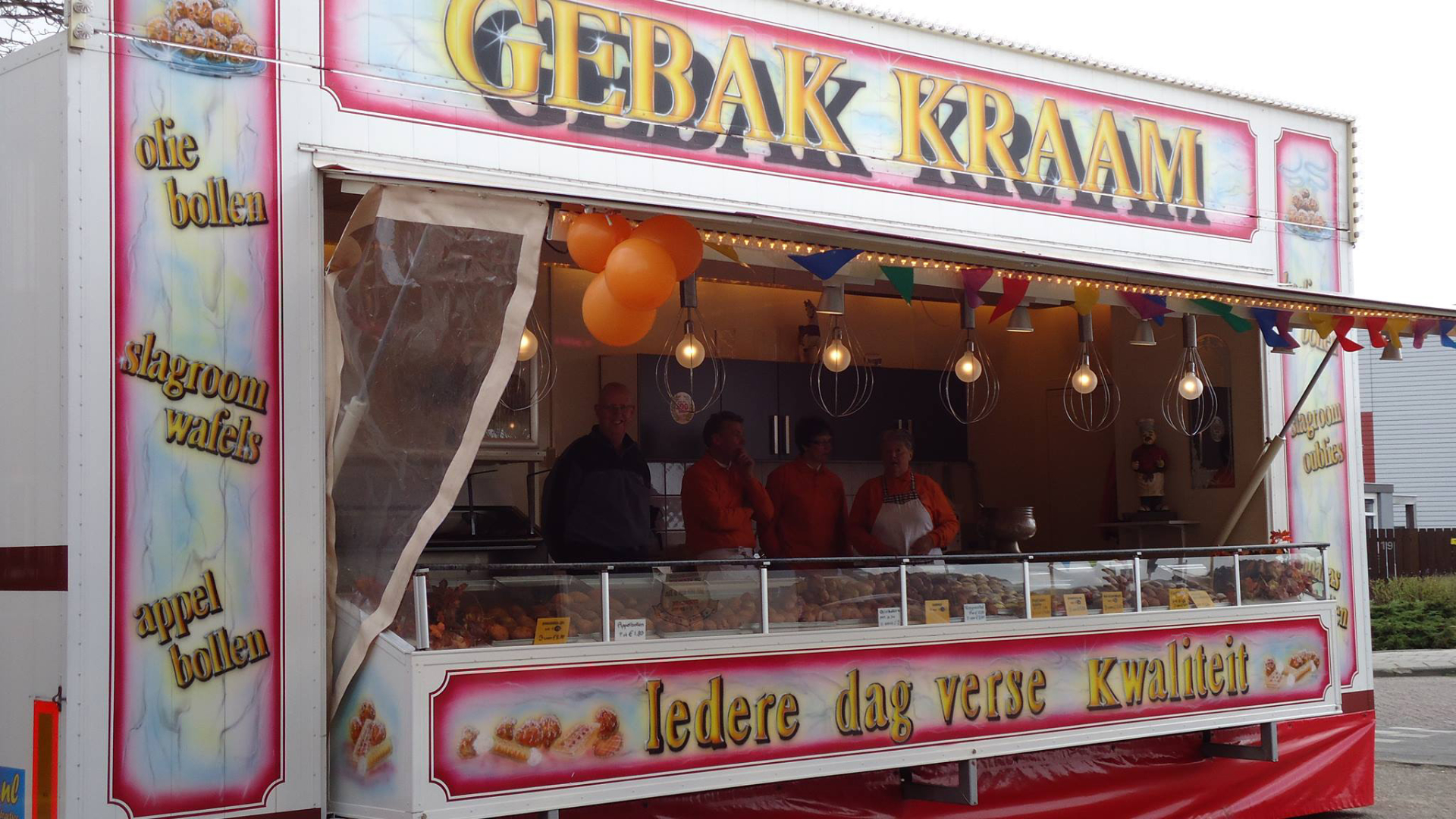 Een gebakswagen met het opschrift "Gebak Kraam" en "Iedere dag verse kwaliteit" biedt oliebollen, slagroomwafels en appelbollen aan. Vier mensen staan achter de toonbank.