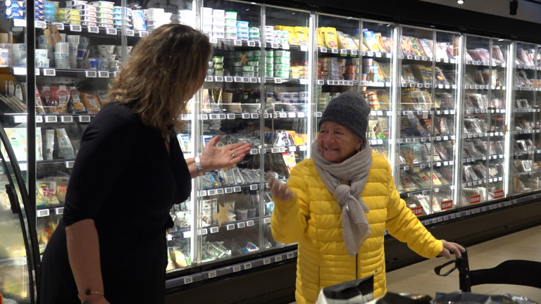 Twee vrouwen in een supermarkt, pratend bij de koelafdeling vol met verpakte producten.