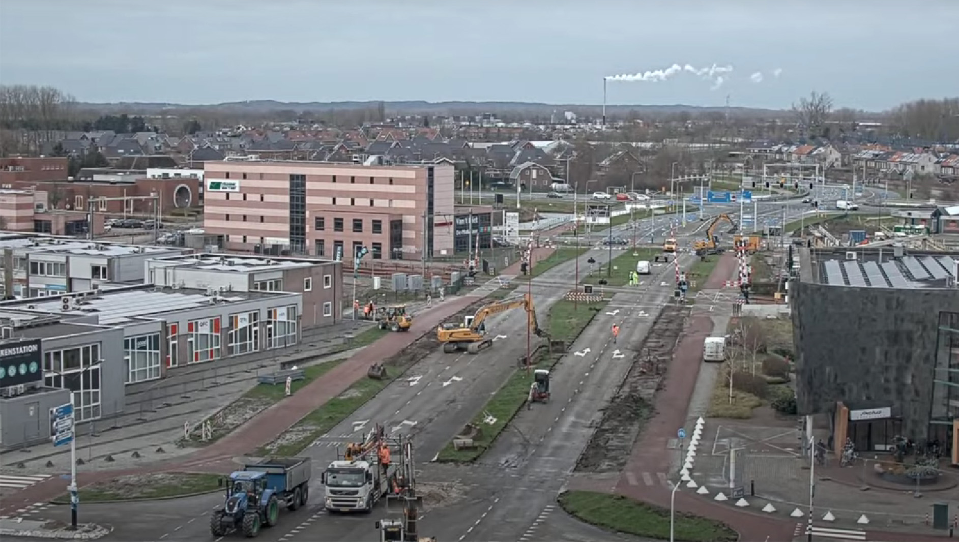 Bouwplaats op een kruispunt met zware machines en werkende arbeiders, omringd door moderne gebouwen.