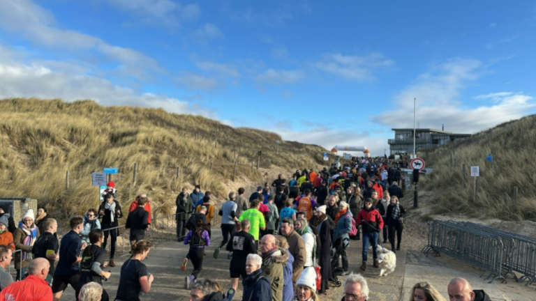 Mensenmassa op een pad tussen duinen onder een blauwe lucht.