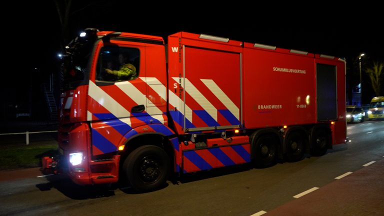 Rood-wit-blauwe schuimbluswagen van de brandweer rijdt 's nachts over een straat.