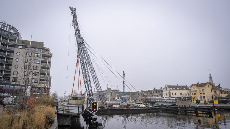 Een hijskraan in werking boven een waterweg met stedelijke gebouwen op de achtergrond.