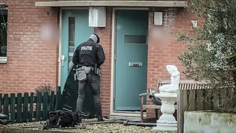 Een politieagent in uniform bij een voordeur van een bakstenen huis.