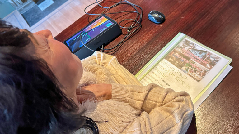 Vrouw leest een document over behoud Stadsstrand De Kade in Alkmaar, met een computer en muis op tafel.
