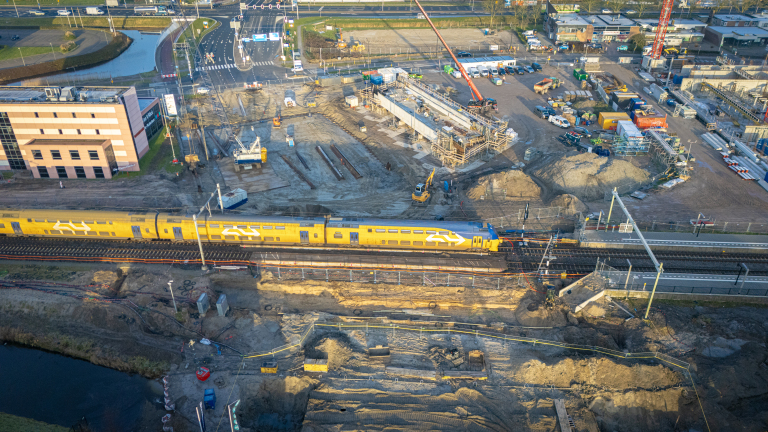 Luchtfoto van een trein die door een bouwplaats rijdt, met bouwvoertuigen en materiaal verspreid over de site.