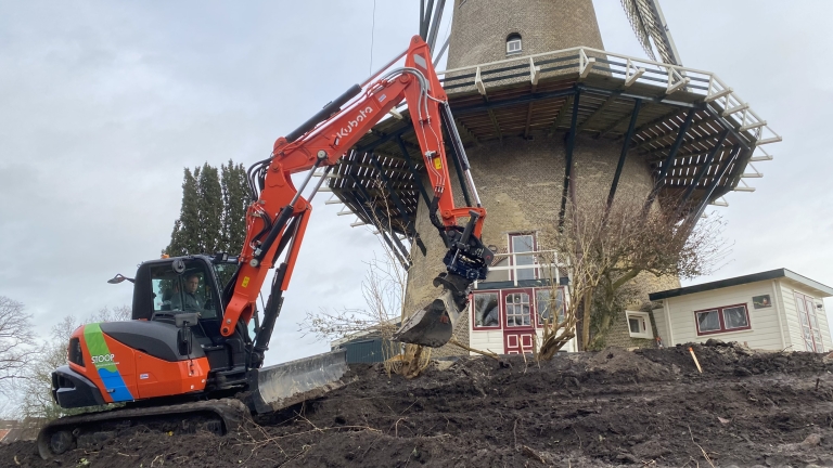 Graafmachine aan het werk naast een oude windmolen.