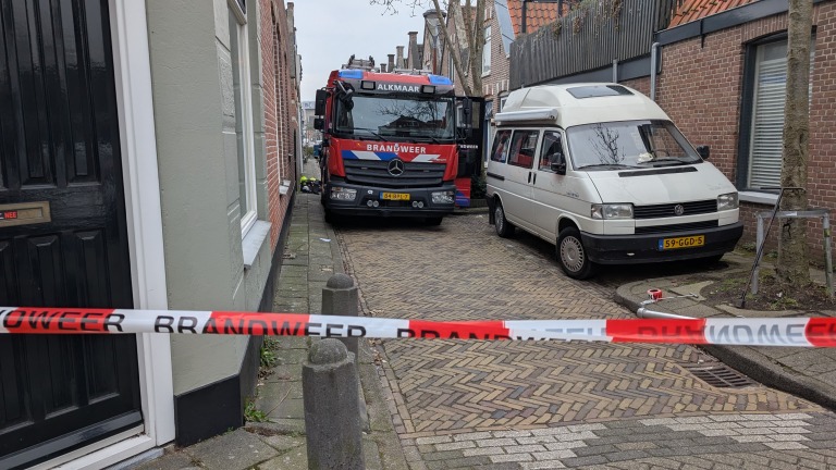 Brandweerwagen en bestelwagen in smalle straat, met brandweerafzetting.