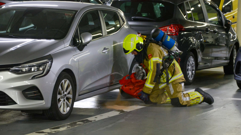 Brandweerman in een parkeergarage bezig met werkzaamheden bij een geparkeerde auto.