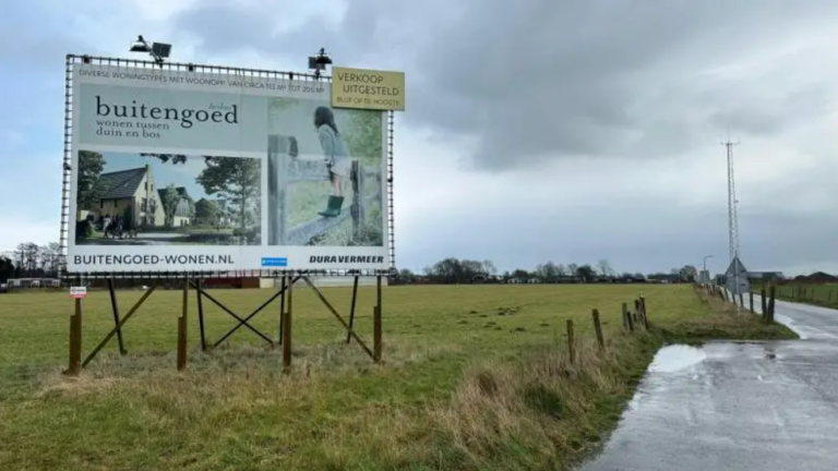 Een groot billboard op een grasveld met een advertentie voor "Buitengoed" woningen. Op de achtergrond is een grijsbewolkte lucht en een lange weg.