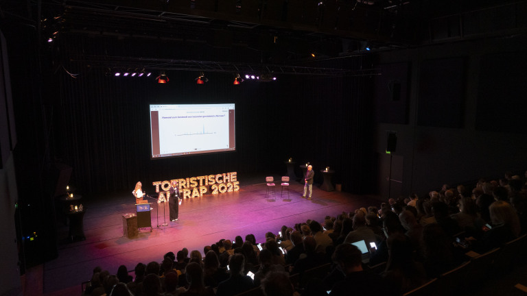 Een presentatie in een theaterzaal met een scherm en de tekst "Toeristische Altrap 2025" op het podium.