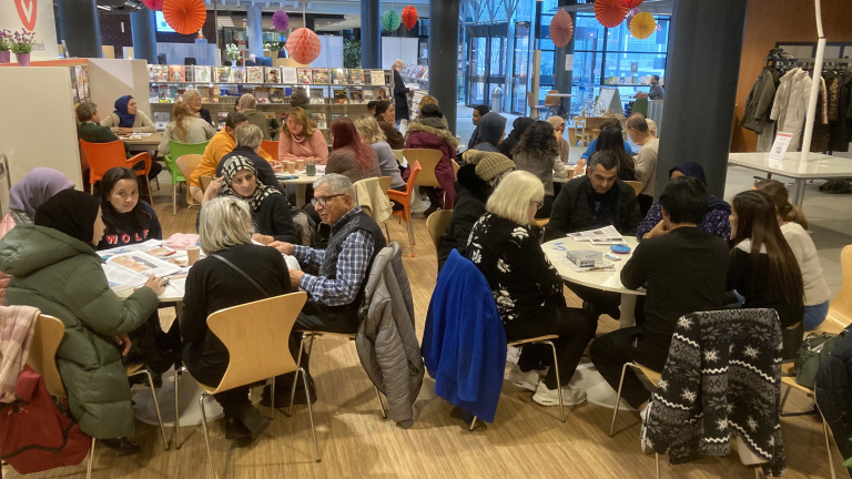 Mensen zitten aan tafels in een bibliotheek en lezen of hebben een gesprek.