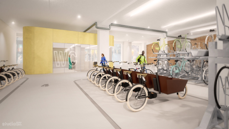 Modern fietsenstalling met bakfietsen, standaard fietsen en een geel wandgedeelte met 'WC' aanduiding; mensen bewegen door de ruimte.