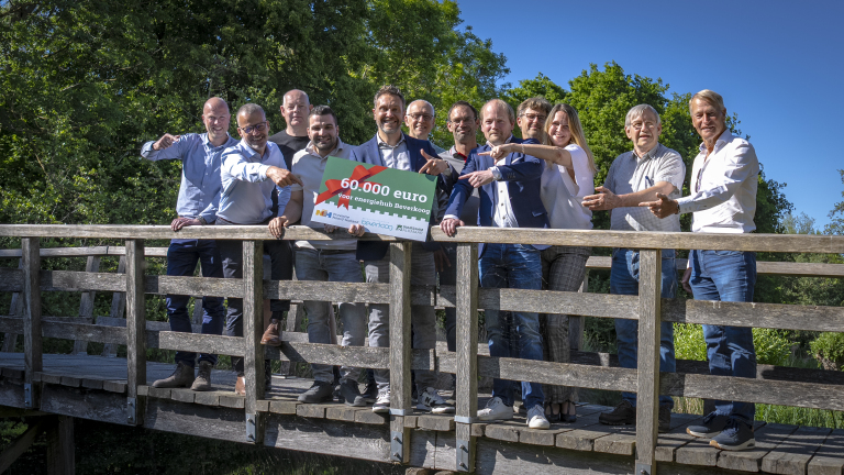 Een groep mensen staat op een houten brug en houdt een bord vast met de tekst '60.000 euro voor energiehub Beverkoog'.