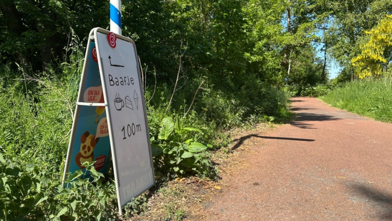Een pad door een groen bos met een bord aan de zijkant dat "Baafje 100m" aangeeft, naast afbeeldingen van een kom soep en een ijsje.
