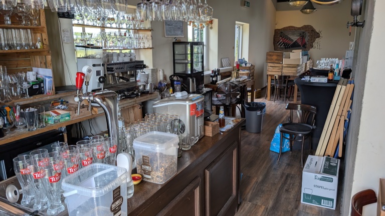 Interieur van een bar met glazen op een rek en de bar zelf vol glazen en apparatuur, waaronder een biertap met Texels-logo en een koffiemachine.
