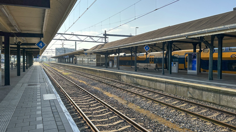 Leeg treinstation met perron 4, spoorrails en een geel-blauwe trein onder overkappingen