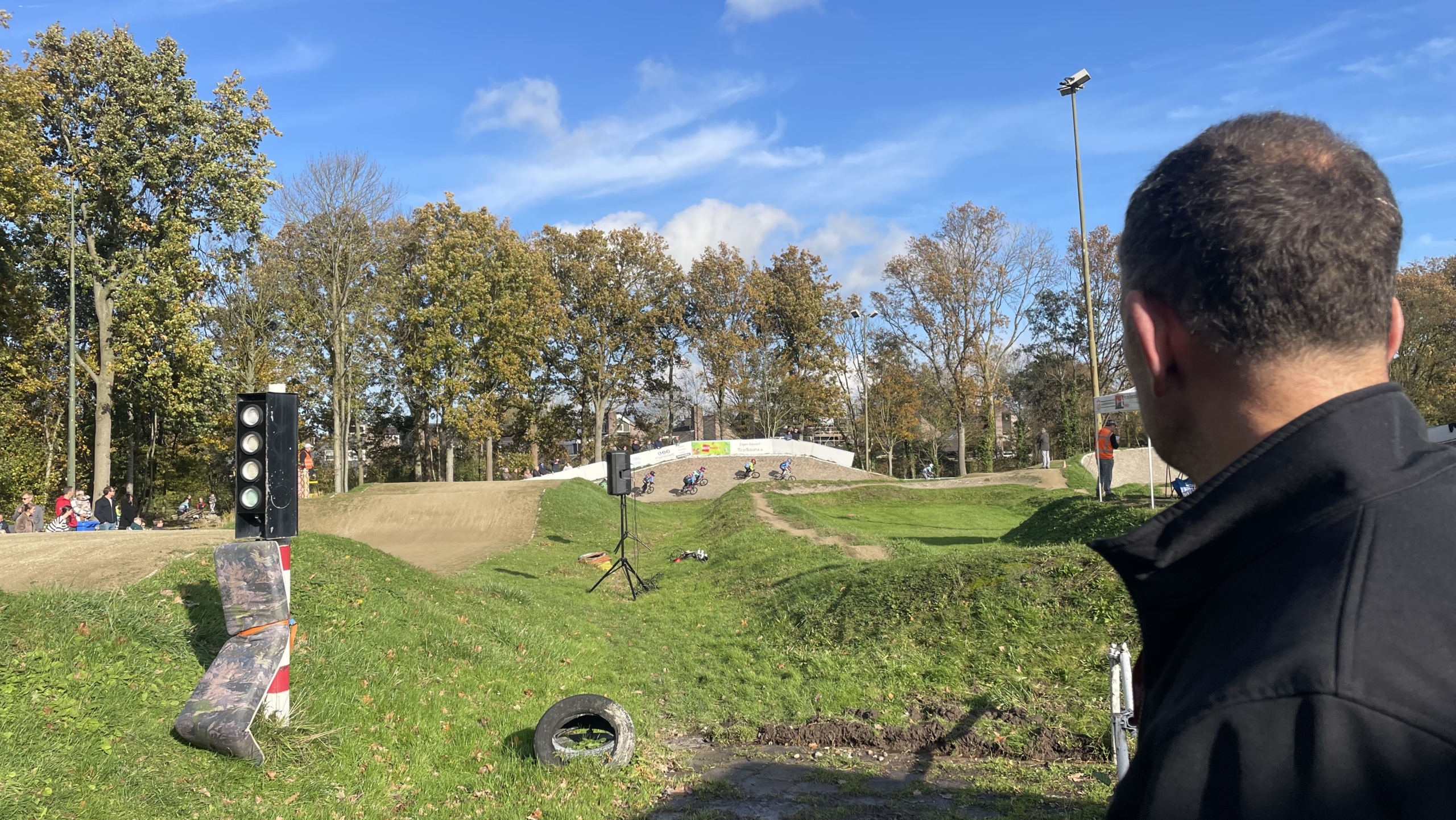 Man kijkt naar een BMX-baan in een park omringd door bomen met een heldere blauwe lucht.