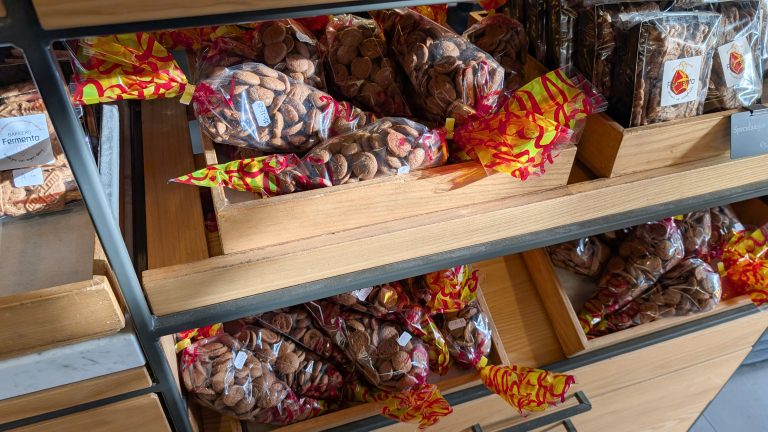 Houten rekken met zakken gevuld met strooigoed en speculaasjes in een winkel, met kleurige verpakkingen.