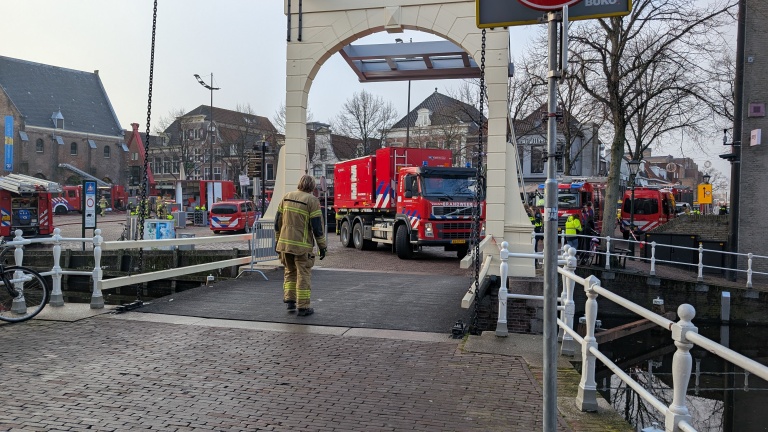 Een brandweerman loopt naar een rode brandweertruck die door een brug rijdt, omringd door meerdere brandweer- en hulpdienstvoertuigen in een stedelijke omgeving.