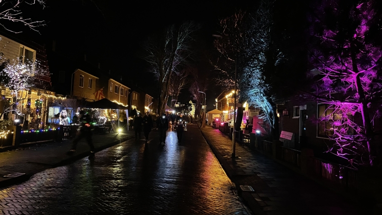 Verlichte straat in de nacht met huizen versierd met kleurrijke kerstverlichting en voorbijgangers die op het trottoir lopen.