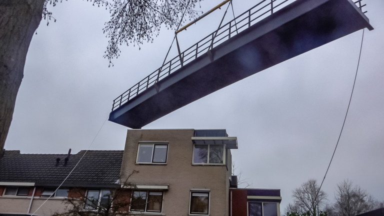 Een brug wordt met behulp van kabels over een huis heen getild.