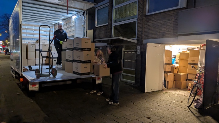 Mensen laden verhuisdozen uit een vrachtwagen en plaatsen ze in een garage vol met dozen, 's avonds op straat.