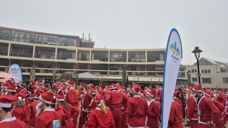 Mensen verkleed als kerstmannen verzamelen zich buiten bij een gebouw met een feestelijke sfeer.