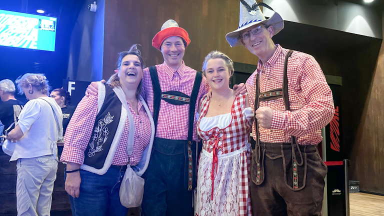 Vier mensen in traditionele Beierse kleding met geruite overhemden en hoeden, lachend en poseren voor de camera.