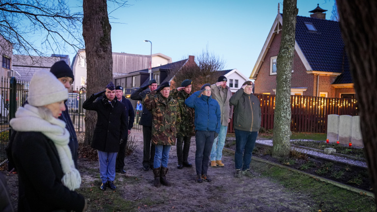 Een groep mensen, waaronder mannen in militaire uniformen, brengt een saluut bij een gedenkteken op een begraafplaats.