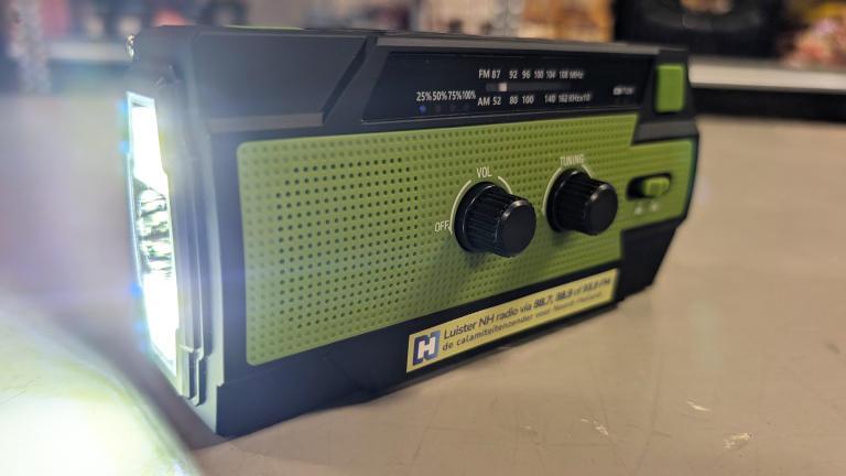 Groene draagbare radio met volumeknop en afstemknop, met een ingeschakelde zaklamp aan de linkerzijde.