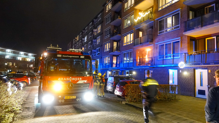 Brandweerwagens en brandweerlieden bij een brandend appartementencomplex 's nachts, met rook en noodverlichting zichtbaar.