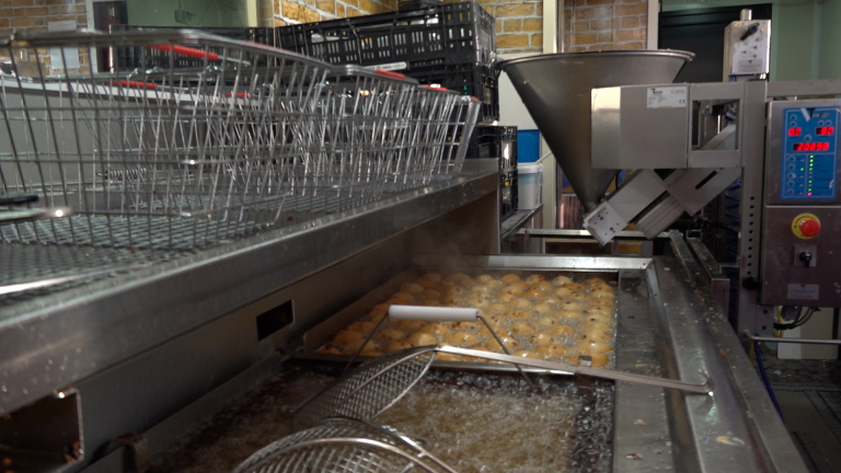Automatische machine bakt oliebollen in een friteuse in een industriële keuken.