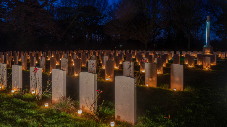 Een begraafplaats verlicht door kaarsen bij nacht, met rijen grafstenen en bloeiende rozen.