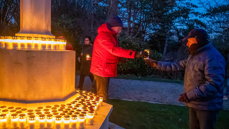 Mensen verlichten kaarsen bij een gedenkteken in de schemering.