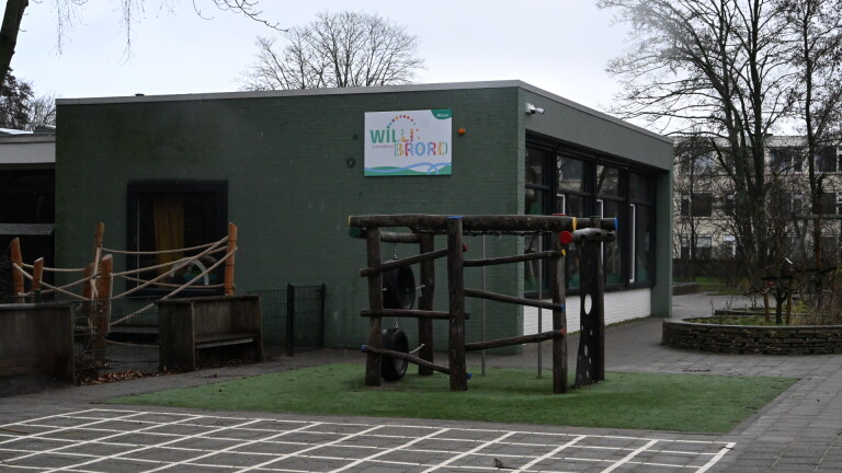 Een groen gebouw met speeltoestellen buiten en een bord met de naam "Willibrord" erop.