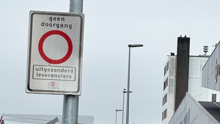 Verkeersbord met een rood-witte cirkel en tekst "geen doorgang, uitgezonderd leveranciers" tegen een stedelijke achtergrond.